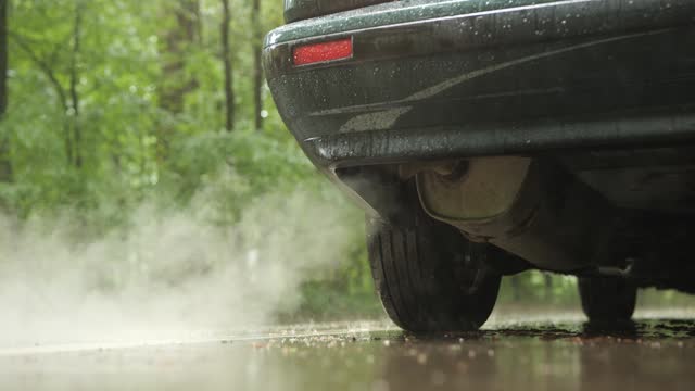 Exhaust fumes or smoke coming out of a car's tailpipe. Low angle view, rainy summer day, no people