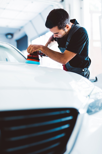 Car detailing and polishing done by service man in workshop.