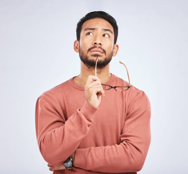 Entscheidung, Denken und asiatischer Mann im Studio mit Brille, Fragen und Brainstorming auf grauem Hintergrund. Warum, Idee und männliche Person mit Emoji, Körpersprache oder Wahlgeste, verwirrt oder Lösung – Foto