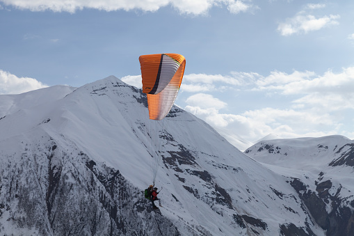 Gudauri, Georgia - May 1, 2019: Paragliders flying in front of snowy peaks of Caucasus on a sunny day
