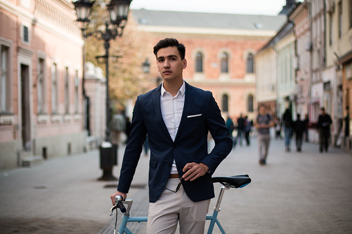 Elegant businessman in stylish suit with a blue bicycle outdoors on the street.