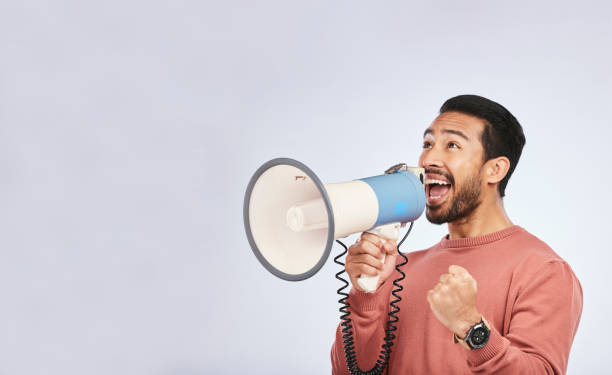 istock Megaphone, man and shout in studio space, white background and broadcast speech, announcement and mockup. Asian model, microphone and advertising sales, news and attention of deal, promotion or offer 1550589744
