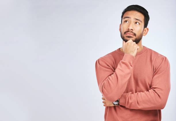 Man, thinking and idea mockup in studio or planning, decision and choice with white background. Asian male, model and curious face with doubt, questions or confused guy try to remember with space