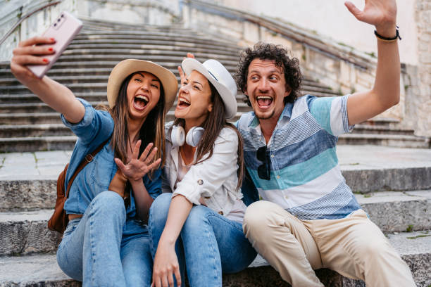 istock Three Young Friends Sitting On The Steps In Dubrovnik And Taking Selfies 1550666486