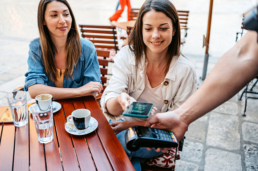 Young woman paying the bill via contactless channel by mobile banking application in a sidewalk café in Dubrovnik, Croatia.