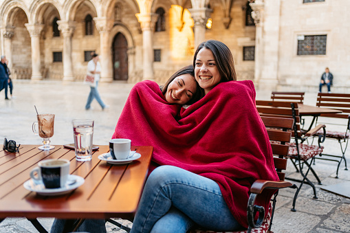 Two young female friends covered with a blanket while sitting in a sidewalk café in Dubrovnik, Croatia.