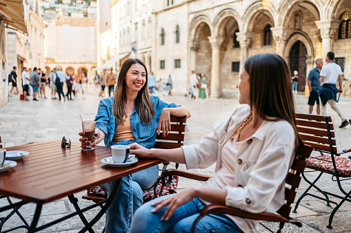Two young female friends drinking coffee in a sidewalk café in Dubrovnik, Croatia.