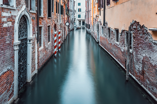 Narrow water canal and red brick worn out buildings built on water in Venice, Italy. Long exposure photography.