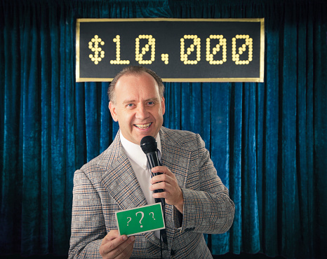 A vintage color processed game show host holding a microphone. Photographed in studio with a purpose built set and props.