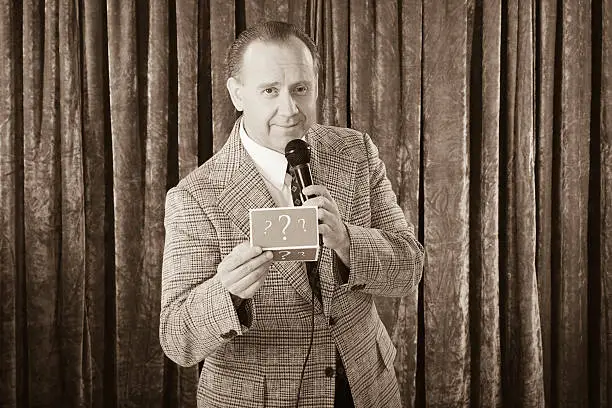 A vintage processed game show host holding a microphone. Photographed in studio with a purpose built set and props.
