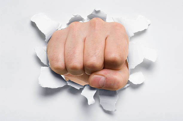 istock Fist punching through a ripped hole in a paper 155074135