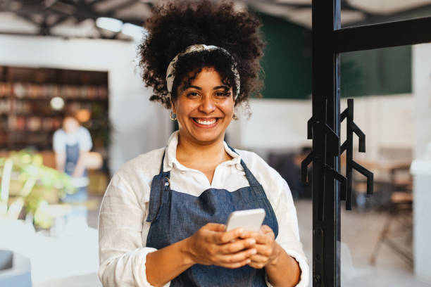 exitosa dueña de una cafetería usando su teléfono en su cafetería - restaurant wireless technology office worker business fotografías e imágenes de stock