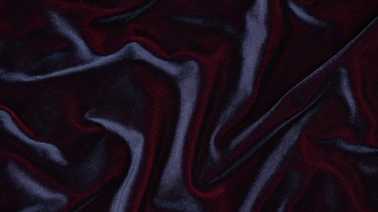 closeup of soft folds of shiny iridescent burgundy velvet fabric with blue shades. slow rotation.