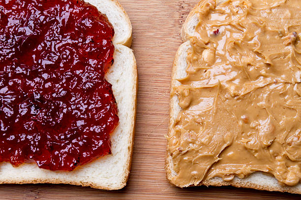 Peanut Butter and Jelly Sandwich Fancy Lunch Classic kids lunch of peanut butter and jelly sandwich wrapped and tied elegantly in a paper wrapper.  Sandwich is on a retro blue plate on a cutting board with peeled baby carrots, green grapes and cinnamon topped apple sauce in a round white ramekin. peanut butter and jelly sandwich stock pictures, royalty-free photos & images