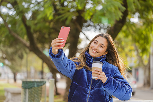 Latin girl taking a selfie with her mobile phone in a public park.