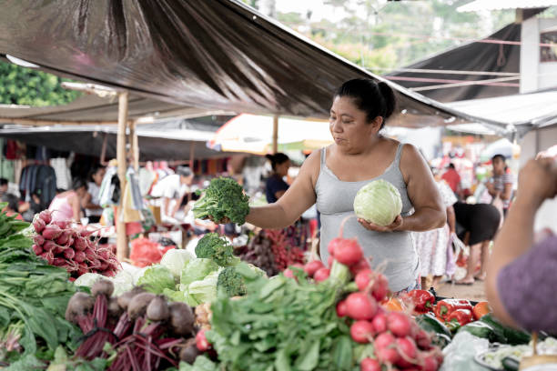 uma mulher hispânica adulta está segurando uma couve-flor e um brócolis em um mercado de rua - horizontal guatemala leaf vegetable market - fotografias e filmes do acervo
