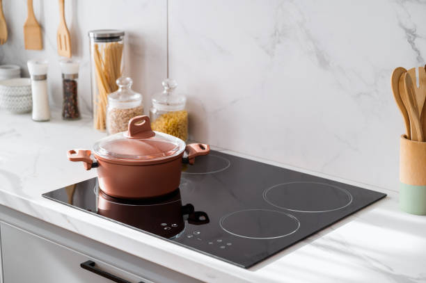 Clean black induction stove with control panel near marble countertop Clean new and black induction stove with control panel near marble countertop on white kitchen. Metal saucepan and jars with products on cooking surface. Cookery and homemade food concept burner stock pictures, royalty-free photos & images