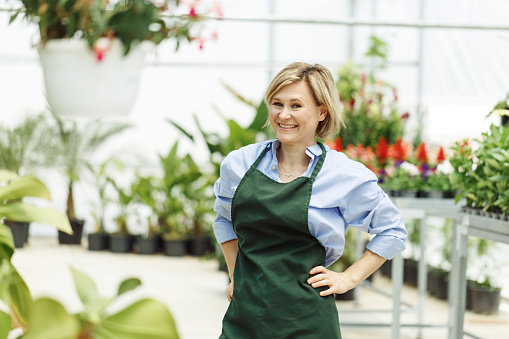 Woman is owning small business greenhouse store. Female entrepreneur in green apron