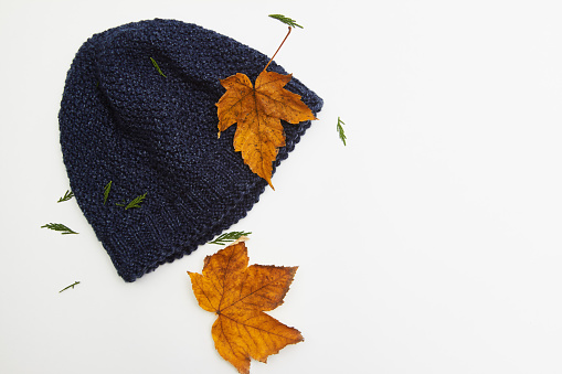 Autumn composition; Autumn leaves and knit hat on white background with copy space. Flat lay, top view