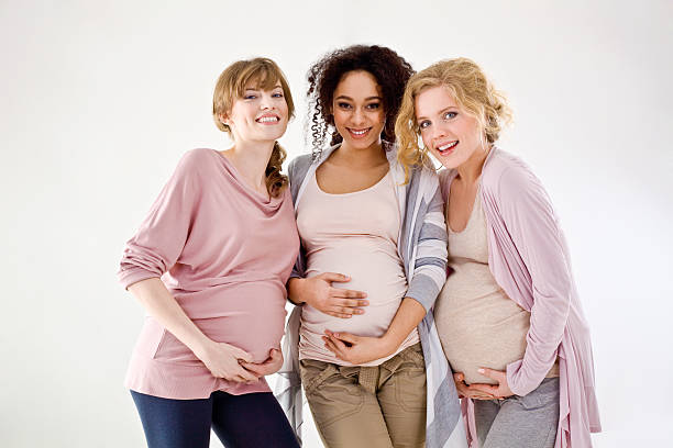 multicultural pregnant women sitting close together, touching bellies isolated on grey