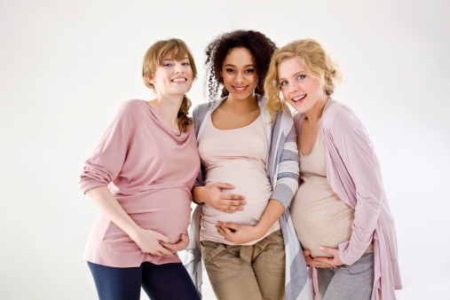 Smiling young women couple next to living room window. Tender touching partner's pregnant belly. Woman's health, happy pregnancy doula supporting, same-sex marriage and calm mental mood concept image.