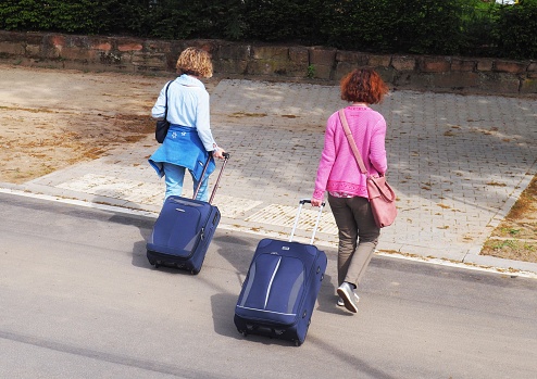 Wixhausen, Germany – May 07, 2023: Two female travelers, walking side by side on a roadway, each with a rolling suitcase
