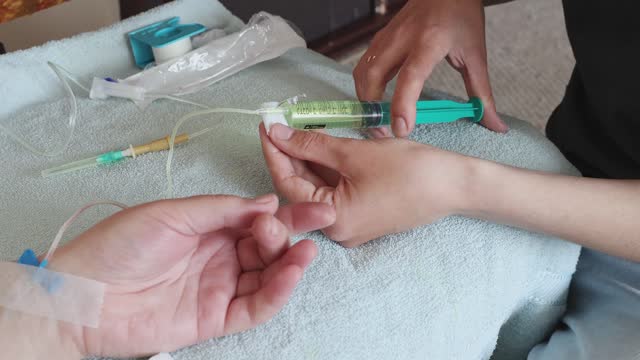The nurse injects medicine through an IV drip into a patient's vein at home.