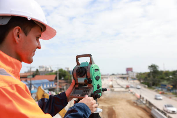 istock Site young man engineer operating his instrument during roadworks looking at a survey camera. Builder using total positioning station tachymeter on construction site for new road setting outside 1550812255