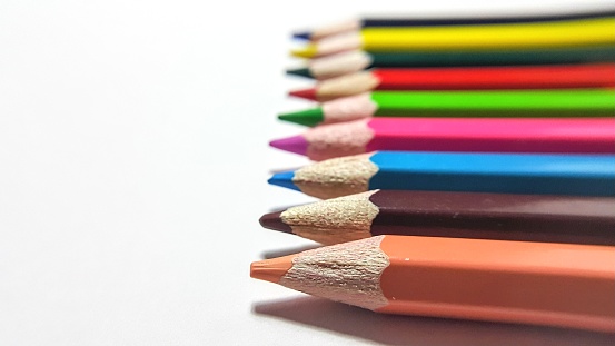 Wooden artists rainbow of drawing pencil crayons are laying in a straight diagonal line on a white marble background with copy space above them.