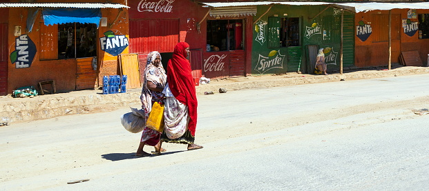 Harar, Ethiopia - January 11, 2023: Muslim women walk in the roads of Harar, carrying water in plastic tank and big sacks. Harar emerged as the center of Islamic culture and religion in the Horn of Africa during end of the Middle Ages.