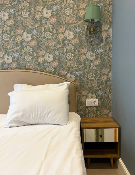 istock Close-up fragment of bedroom with empty bedside table, reading lamp and socket in modern interior​ design home or hotel. Soft pillow and blanket, stylish comfortable furniture. 1550843112