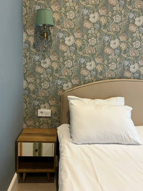 istock Close-up fragment of bedroom with empty bedside table, reading lamp and socket in modern interior​ design home or hotel. Soft pillow and blanket, stylish comfortable furniture. 1550843650