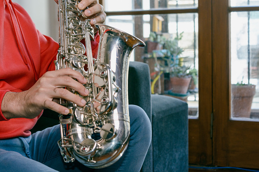 closeup in profile with copy space of caucasian male hands of unrecognizable man sitting on the sofa playing a saxophone inside home.