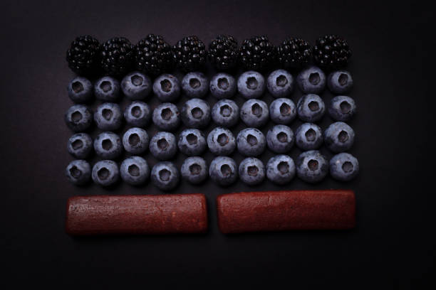 A balanced pattern of laid out blueberries, blackberries, and berry bars. On a black background.