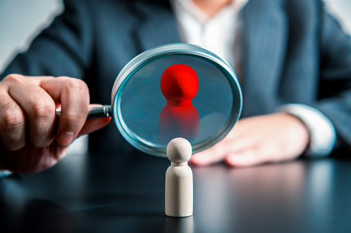 Businessman using magnifying glass look at company personnel looking for people with high potential and skill talent on black table background. Business strategy Human resources recruitment concept.