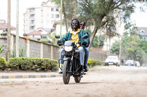 Full length view of smiling man and woman riding vehicle powered by smart battery, part of power-swap ecosystem in Nairobi and other rapidly developing cities.