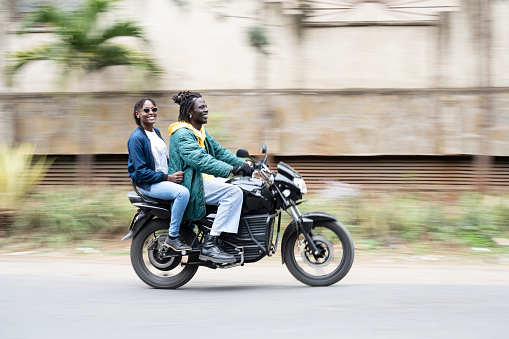 Full length side view of man and woman in 20s and 30s, jeans and jackets, travelling on 350cc bike powered by smart battery embedded with IOT chips.