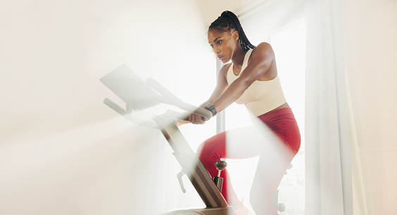 Focused young woman tackling her fitness training head-on, using a digital bike as part of her home workout routine to stay motivated and committed to achieving her fitness goals.