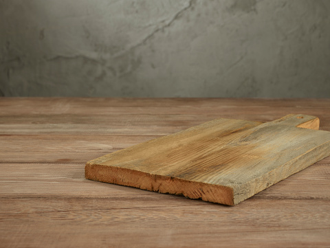 Empty cutting board on a wooden table in front of a concrete wall