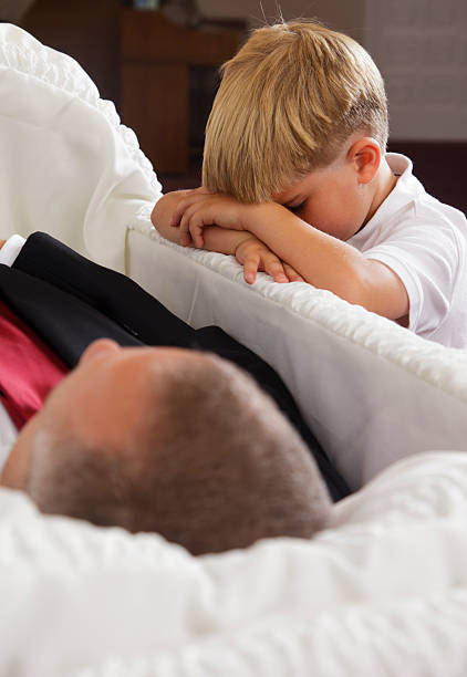 Grieving Little Boy A sad little boy kneeling beside an open casket at a funeral. child casket stock pictures, royalty-free photos & images