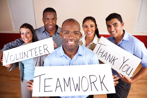 Mixed-ethnic group of young adults in a small group at a business conference. They are holding signs that read Teamwork, Volunteer and Thank You. 