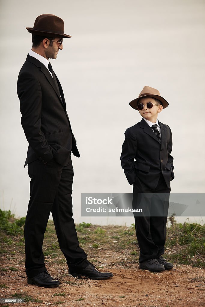 Pai e filho em trajes semelhantes, ao ar livre, a luz do dia, vertical - Foto de stock de Terno royalty-free