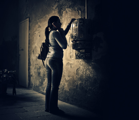 woman using a public pay phone in a dark deteriorated building  in milan, italy