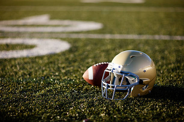 American Football An American football helmet and football on the football field. Perfect image for your football announcement. football helmet and ball stock pictures, royalty-free photos & images