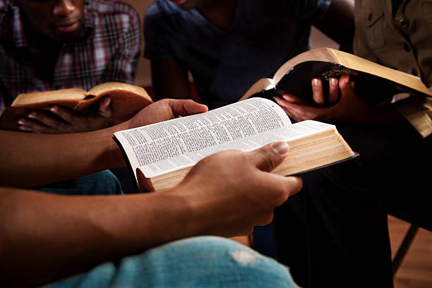Young adults in a Bible study. Young adults meeting together in a Bible study.  Focus on the Open Bible.    bible stock pictures, royalty-free photos & images