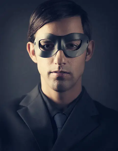 young man wearing all black - shirt, suit and tie, wearing a dark mask an staring at camera