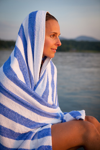 A young woman is wrapped up in a towel, and contemplating the last daylight as the sun sets.