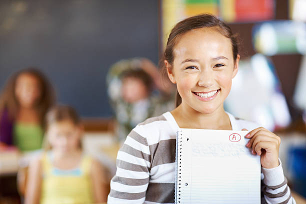 Sweet girl holding paper Portrait of sweet girl holding paper with classmates sitting in background good grades stock pictures, royalty-free photos & images