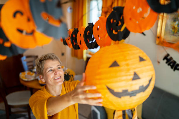 A woman hanging a jack o' lantern halloween decoration A woman is reaching up to hang a paper jack o' lantern while decorating a room ready for a halloween party halloween pumpkin decorations stock pictures, royalty-free photos & images