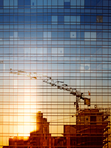 Reflection of a construction site with a crane  in windows of a modern office building in sunset